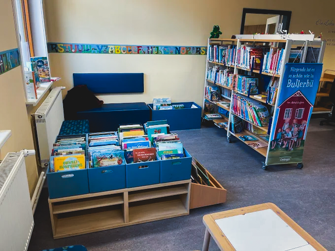 Innenfoto der Bücherei Thiede, es ist die Kinderecke mit einer Sitzgelegenheit und einer Variation von Ablagen für Kinderbüchern inkl. der Bücher zu sehen
